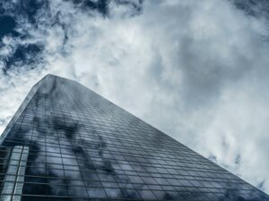 Low angle view of a towering modern skyscraper with glass windows reflecting clouds against a dramatic sky.